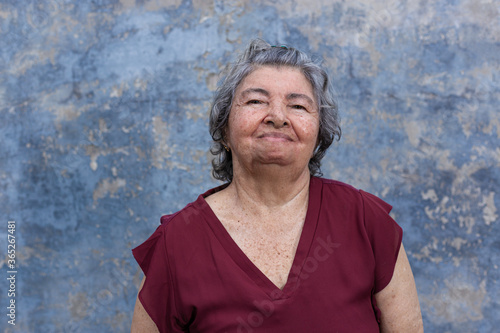Portrait of an elderly woman dressed a wine color blouse with a blue rustic wall background