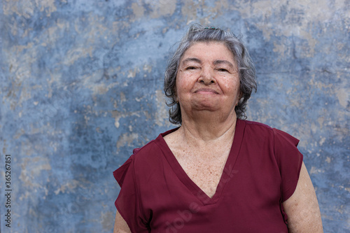 Portrait of an elderly woman dressed a wine color blouse with a blue rustic wall background