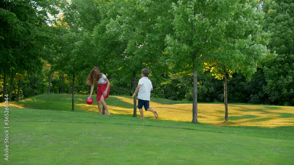 Fototapeta premium Mother and children playing with ball in meadow. Family enjoying time outside