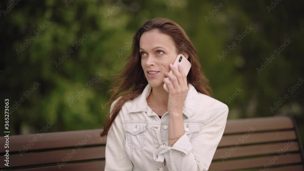 Pretty woman is talking on cell phone in the summer park Pretty woman is talking on cell phone in the summer park