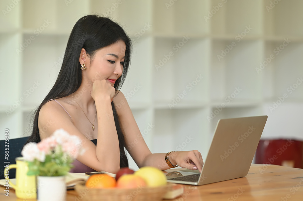 An Asian woman is using a computer laptop while sitting at the wooden working desk. An Asian woman is using a computer laptop while sitting at the wooden working desk.