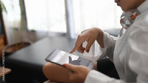 Cropped image woman is using a computer tablet while lying on the sofa in the living room.