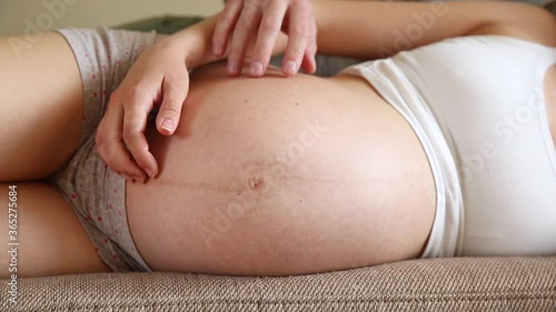 Beautiful pregnant woman and her handsome husband hugging the tummy while in light room.