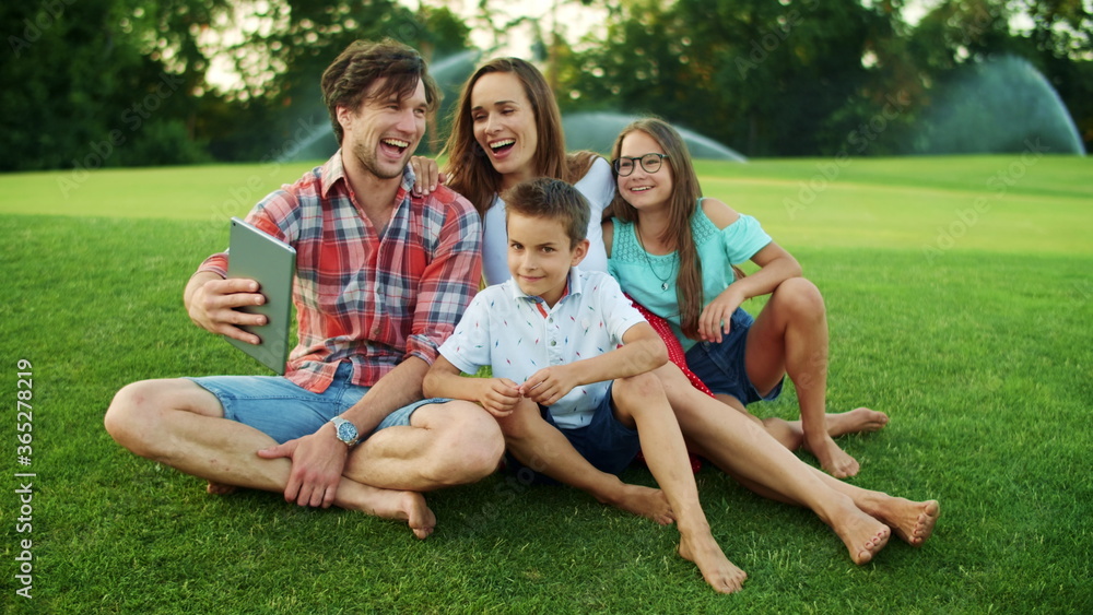 Family laughing together in park. Family having video chat on pad in meadow Family laughing together in park. Family having video chat on pad in meadow