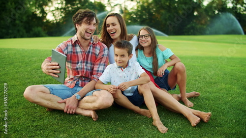Family laughing together in park. Family having video chat on pad in meadow