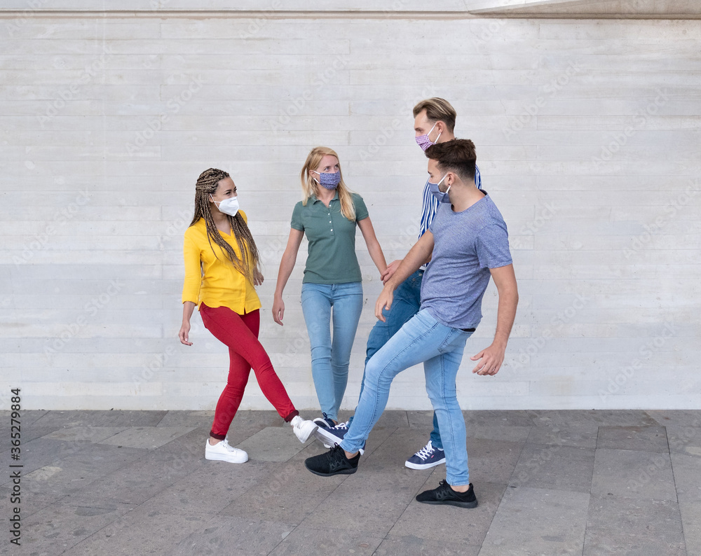Obraz premium Happy multiracial friends meet and greet each other with their feet - Young people wearing protective face mask - Concept of social distance, safety measures and health care