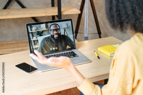 Back view of biracial girl talks via video call with an african-american male colleague or friend on laptop screen. Video call concept
