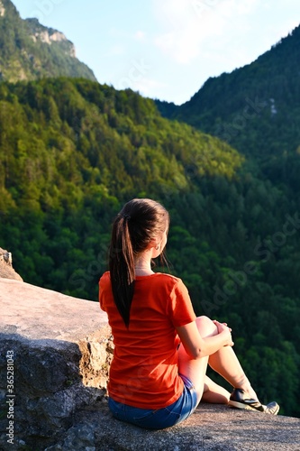 Woman sitting on a stone watching a mountainous landscape.