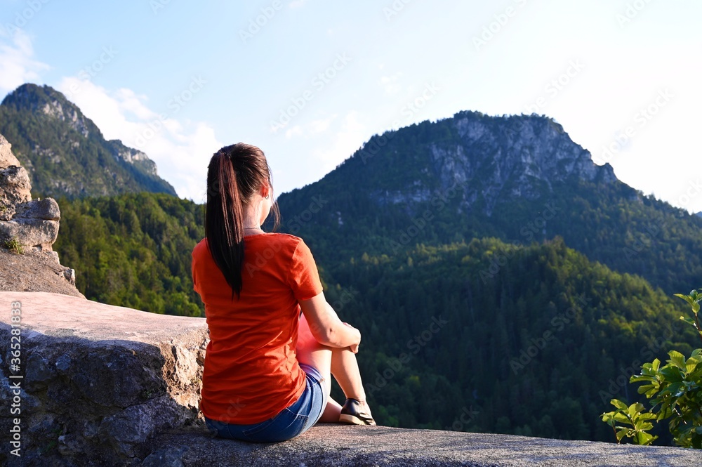 Young woman sitting on stone watching alpine landscape.