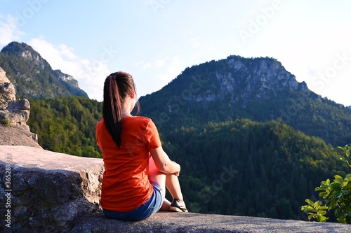 Young woman sitting on stone watching alpine landscape.