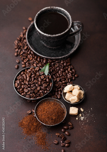 Cup of fresh raw organic coffee with beans and ground powder with cane sugar cubes with coffee tree leaf on brown background. Top view