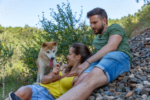 A young couple and a dog sitting over some stones in the mountain