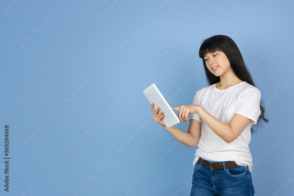 Scrolling tablet, surfing. Portrait of young asian woman isolated on blue studio background. Beautiful cute girl in casual. Human emotions, facial expression, sales, ad, online shopping concept. Scrolling tablet, surfing. Portrait of young asian woman isolated on blue studio background. Beautiful cute girl in casual. Human emotions, facial expression, sales, ad, online shopping concept.
