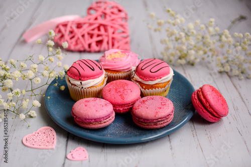 Pink macaroons and pastries on a blue plate on a light wooden background