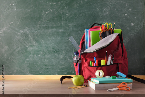 Backpack full of school supplies on table and blackboard front