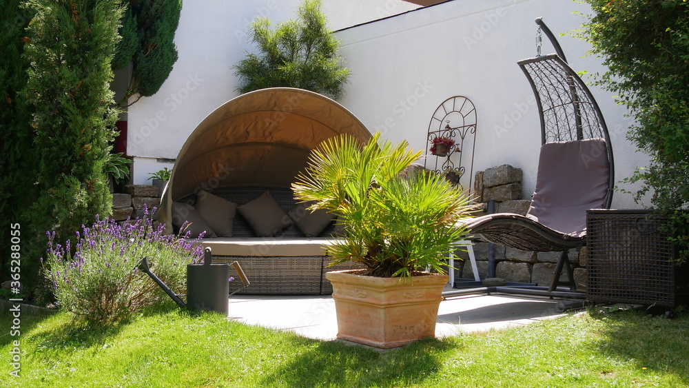 Naklejka premium Gartenterrasse mit Loungegruppe und Hängesessel in einer Gartenecke mit Säulen-Faulbaum und umgeben von einer Palme und Zypressen
