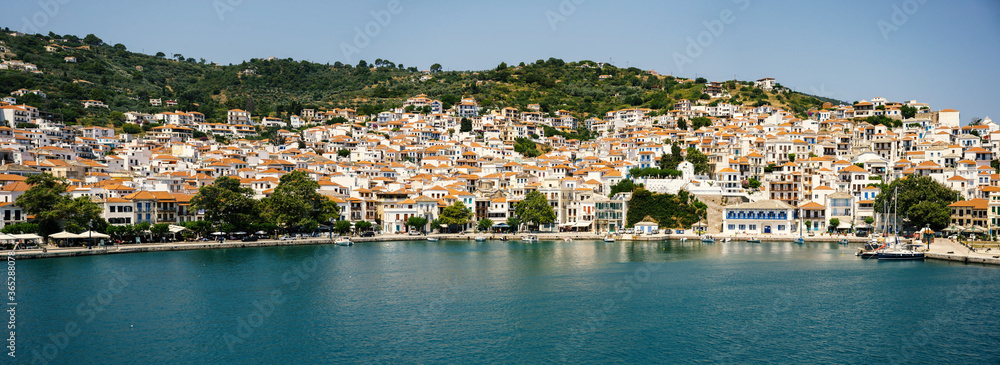 Panoramic view of the historical town on Skopelos island seen from the boat when entering the harbor in summer light.