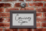 Coming soon. Handwritten inscription in a wooden frame. Brown brick wall