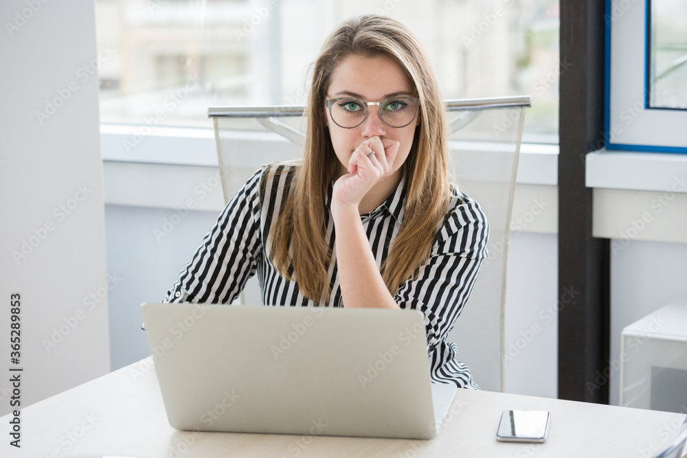 Foto Stock Segretaria bionda con camicia a righe e con occhiali da vista  lavora seduta nella sua postazione di lavoro di fronte al proprio portatile  | Adobe Stock