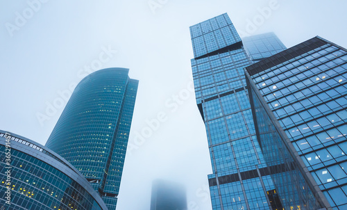 Skyscrapers of the office center made of glass and concrete in clouds of thick fog.