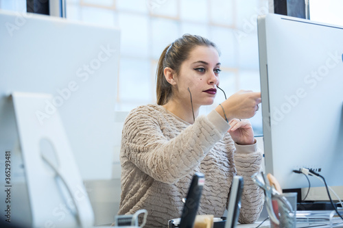 Segretaria, bionda con maglione chiaro lavora davanti al suo monitor seduta nella propria postazione di lavoro di fronte al monitor  