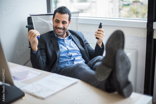 manager moro con giacca nera e camicia blu seduto nella sua postazione lavorativa con i piedi sopra la scrivania nel suo ufficio,  tiene in mano un anti stress per gestire il nervoso ,  photo