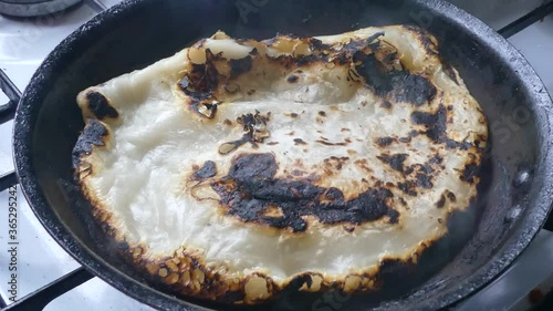 Traditional tasty Indian Partha hot charred smoking pancake cooking on stove in pan dolly left photo