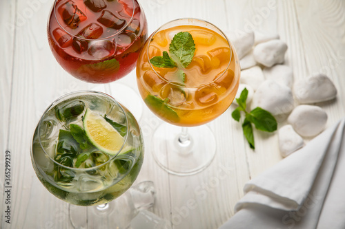 Assorted cold cocktails - mojito, orange and raspberry. On a wooden, white table
