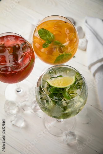 Assorted cold cocktails - mojito, orange and raspberry. On a wooden, white table 