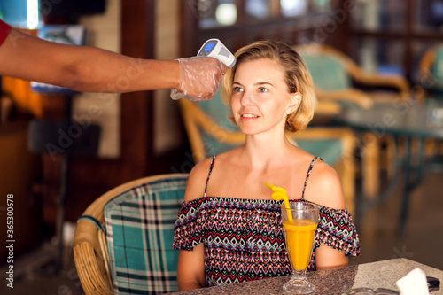 A worker measuring temperature of woman visitior in the cafe. Life during coronavirus time photo