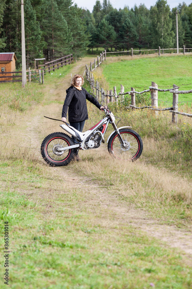 Fototapeta premium Dirt countryside road with mature Caucasian woman standing with motorcycle