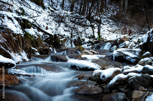 semi frozen small waterfall in a stream in the mountains in deep winter with ice