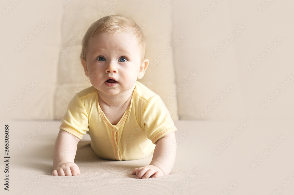 Cute six month old baby lying on his stomach on a bed on a beige background. Soft focus, copy space. Cute six month old baby lying on his stomach on a bed on a beige background. Soft focus, copy space.