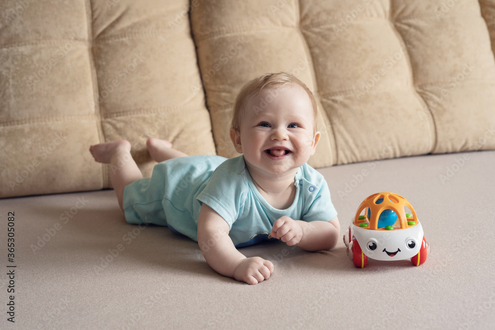 Baby boy lying on his stomach with a toy on a bed on a beige background. Soft focus, copy space. Baby boy lying on his stomach with a toy on a bed on a beige background. Soft focus, copy space.