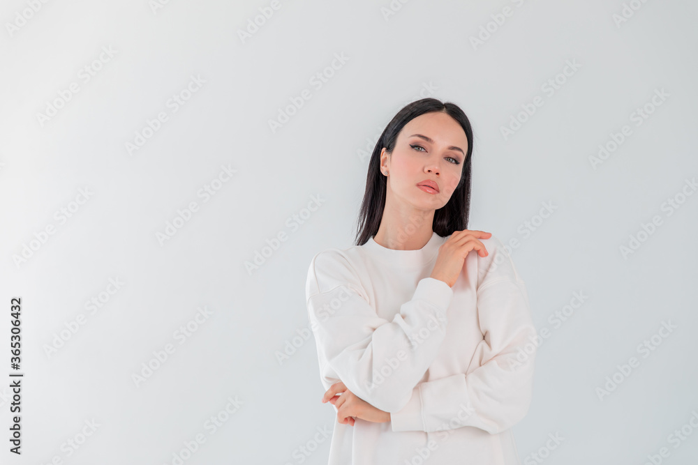 Hipster young girl over wall. Beautiful adult girl model in white sweater hoody isolated over gray white background Hipster young girl over wall. Beautiful adult girl model in white sweater hoody isolated over gray white background