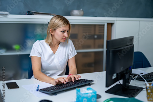 Serious female doctor near computer. Typing diagnosis on keyboard.