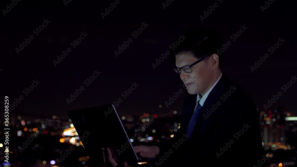 Young Asian businessman entrepreneur using laptop computer with internet working for success business project at office building with city night light background. Business and technology concept. Young Asian businessman entrepreneur using laptop computer with internet working for success business project at office building with city night light background. Business and technology concept.