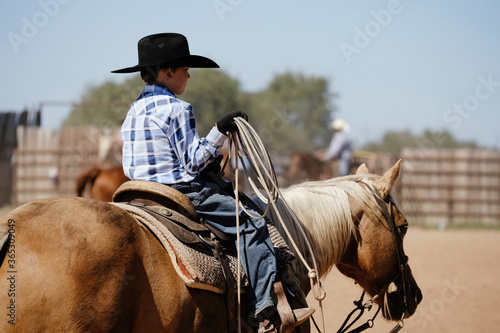 Obraz na plátne Young cowboy in western cowboy hat for ranch lifestyle horseback riding palomino with rope