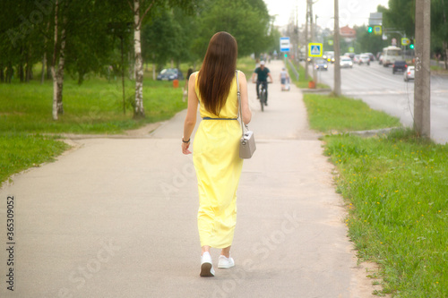 A beautiful girl in a yellow dress is walking along a city street in summer.