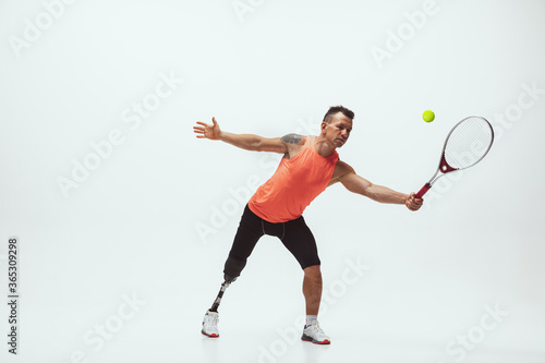 Athlete with disabilities or amputee isolated on white studio background. Professional male tennis player with leg prosthesis training in studio. Disabled sport and healthy lifestyle concept.