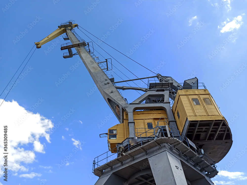 A crane in production. Bottom view of a large crane against the sky. Hoisting machine. A crane in production. Bottom view of a large crane against the sky. Hoisting machine.