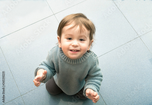 A one-year-old baby kneeling on the kitchen floor, looking at me