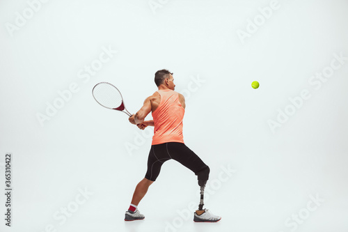 Athlete with disabilities or amputee isolated on white studio background. Professional male tennis player with leg prosthesis training in studio. Disabled sport and healthy lifestyle concept. © master1305
