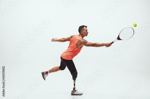 Athlete with disabilities or amputee isolated on white studio background. Professional male tennis player with leg prosthesis training in studio. Disabled sport and healthy lifestyle concept. © master1305