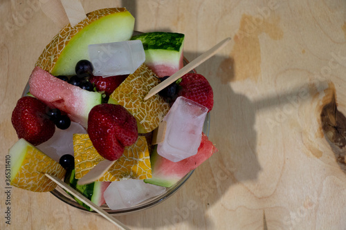 Summer fruit salad with ice in a glass plate. Multi-colored fruits and berries on a wooden background. Healthy snakcs. photo