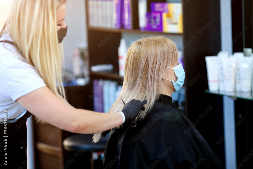 Hairdresser with security measures for Covid-19, a woman in a medical mask, social distance, cutting hair with a medical mask and rubber gloves in a beauty salon. Hairdresser with security measures for Covid-19, a woman in a medical mask, social distance, cutting hair with a medical mask and rubber gloves in a beauty salon.
