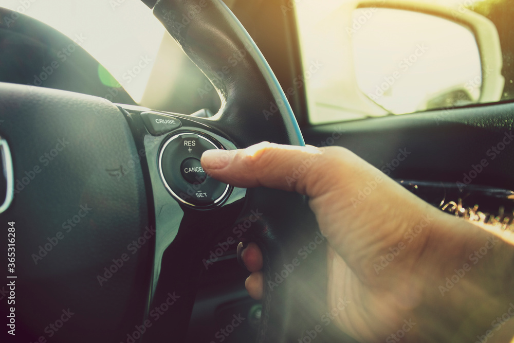 Driver hand pressing to adaptive cruise control  button on steering wheel of a car