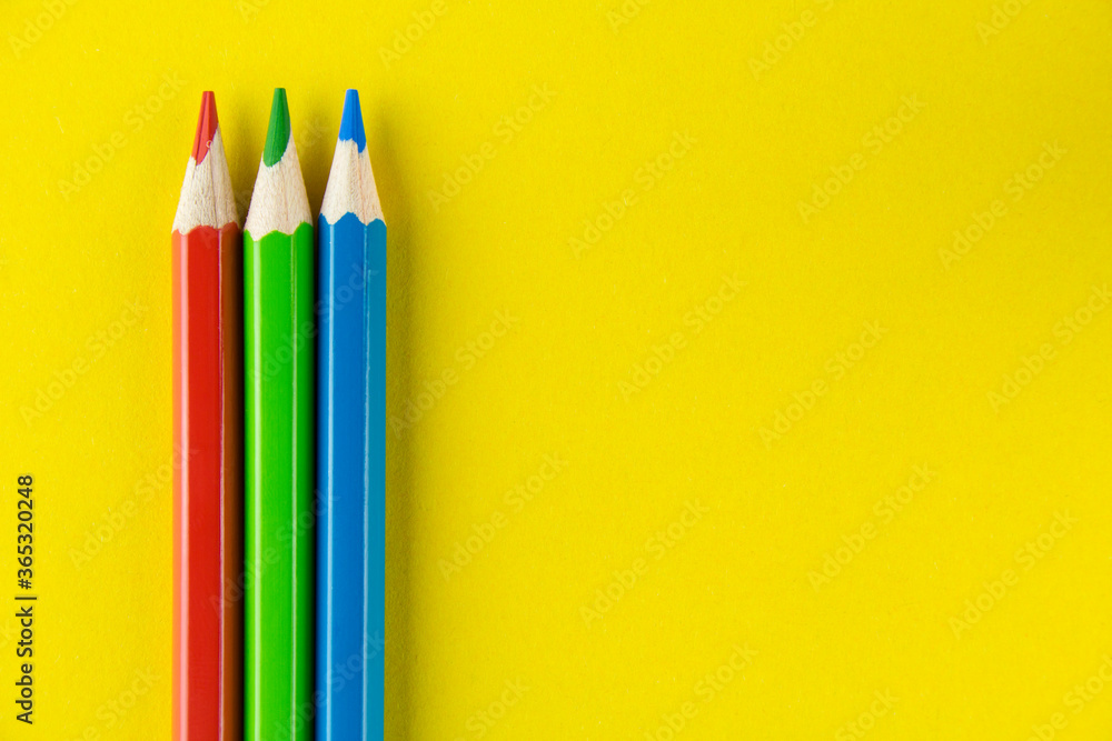 Red, green and blue pencils on yellow background. Copy space for text. Red, green and blue pencils on yellow background. Copy space for text.