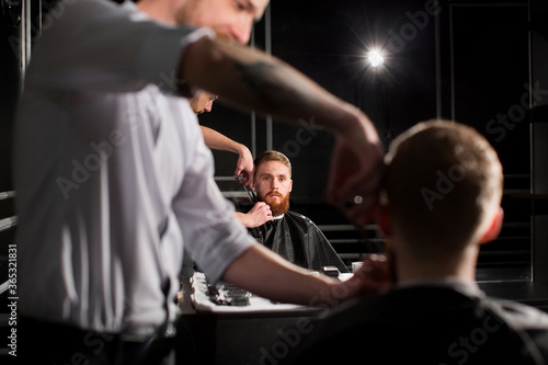 Master cuts hair and beard in the Barber shop. Hairdresser makes hairstyle using scissors and a metal comb.