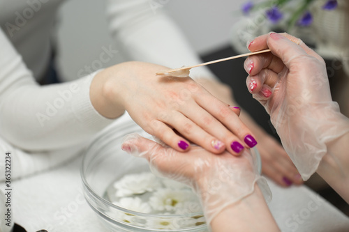 Woman in a nail salon receiving a manicure, she is bathing her hands in paraffin or wax